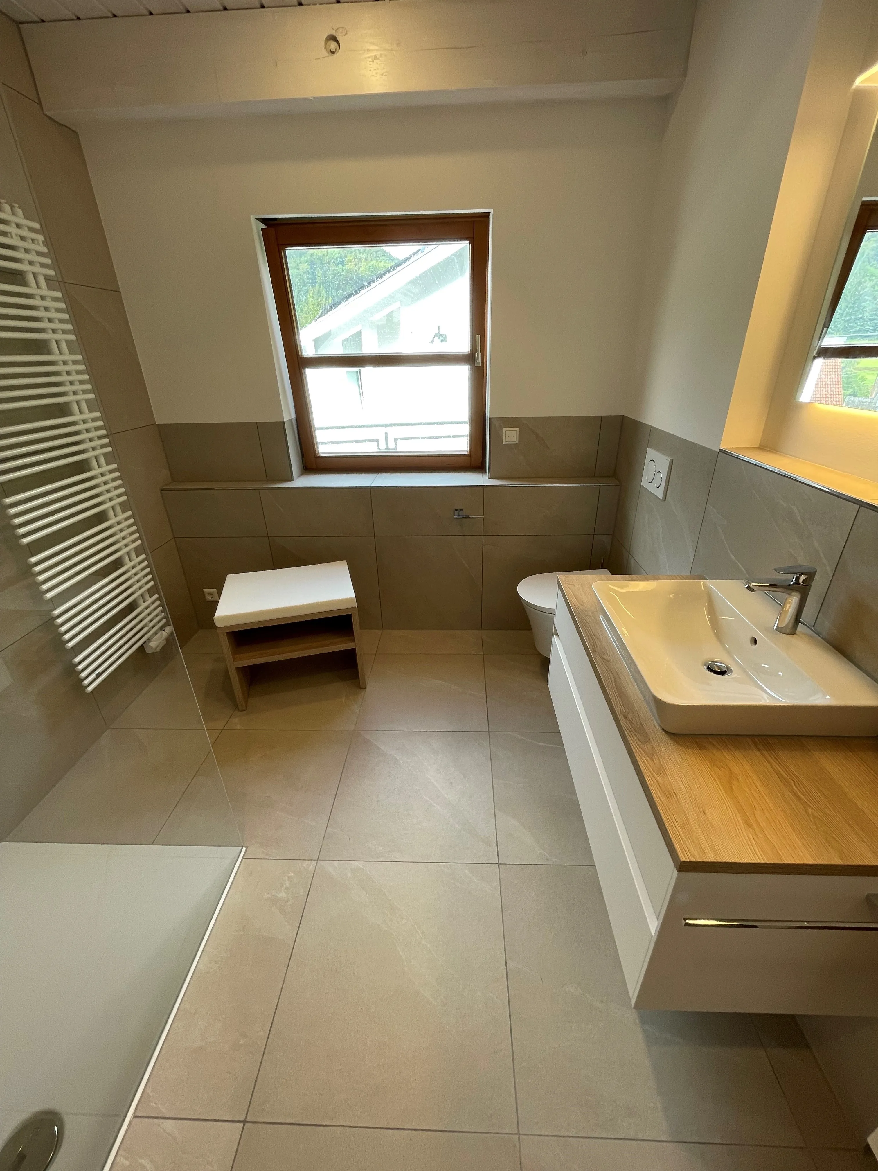 Ein helles, natürlich gestaltetes Badezimmer mit großformatigen beigen Bodenfliesen und Holz-Akzenten.