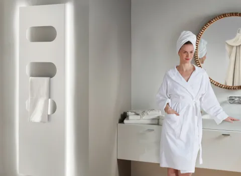 Frau mit Bademantel steht neben LED-Heizkörper PlawaSpa.