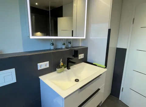 Ein modernes Badezimmer mit einem weißen Waschtisch mit zwei großen Schubladen und einem schwarzen Wasserhahn.