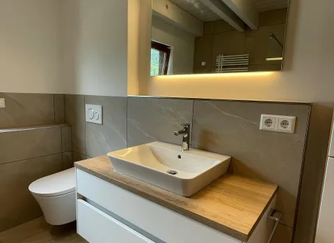 Ein modernes Badezimmer mit einem schwebenden Waschtisch in Weiß und einer Holzplatte, auf der ein eckiges Aufsatzwaschbecken platziert ist.