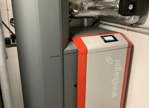 Moderne Pelletheizung der Marke Windhager in einem Heizungsraum, mit isolierten Rohrleitungen und digitalem Steuerungsdisplay.