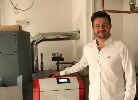 Mann steht neben moderner Heizungsanlage mit Rohrleitungen im Kellerraum.