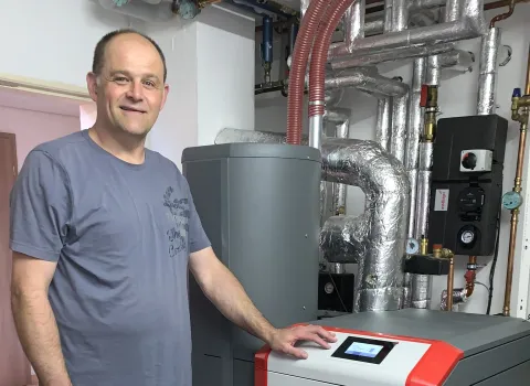 Mann steht neben moderner Heizungsanlage mit isolierten Rohren im Technikraum.