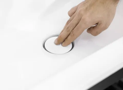 Eine Hand betätigt den Abflussstopfen eines modernen Waschbeckens mit einem Push-open-Mechanismus.