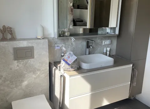 Modernes Badezimmer mit wandhängendem WC, hellem Waschtisch, großem Spiegelschrank und Steinoptik-Rückwand.