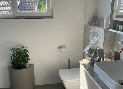 Helles Bad mit wandhängendem WC, Dekoration, Pflanzen und großem Fenster – moderner, minimalistischer Stil.