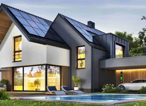 Nachtansicht eines schönen, modernen Hauses mit Sonnenkollektoren, Wallbox und Swimmingpool.