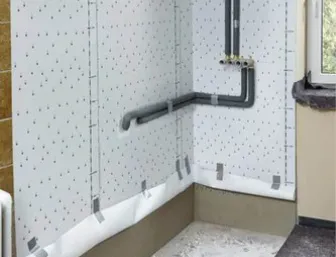 Badezimmer im Sanierungsprozess: Die Wand ist nun mit weißen, wasserfesten Bauplatten verkleidet, in die kleine Markierungspunkte eingedruckt sind.