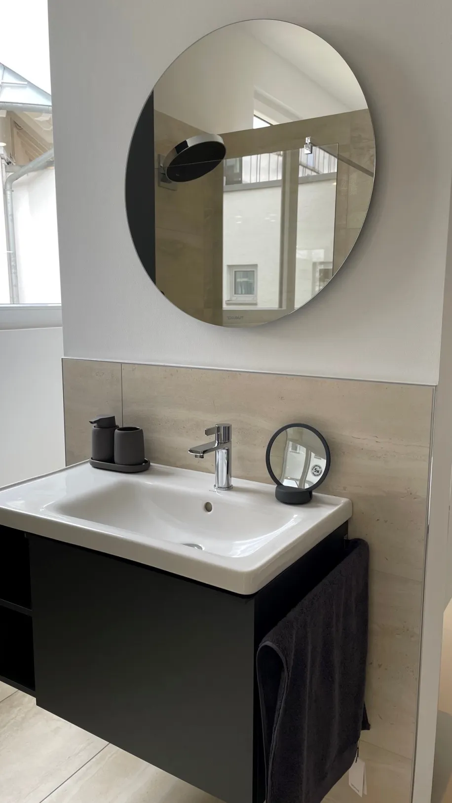 Ein modernes Badezimmer-Waschbecken mit schwarzem Unterschrank ist an einer hellen Wand montiert.