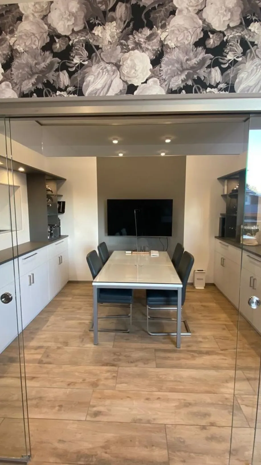 Ein modern eingerichteter Besprechungsraum mit Glastüren zeigt einen rechteckigen Tisch mit sechs dunkel gepolsterten Stühlen.