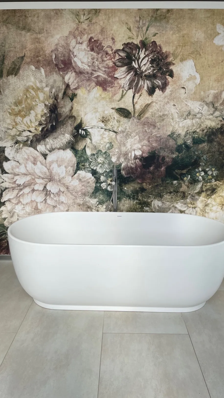 Eine freistehende, weiße Badewanne steht vor einer auffälligen Wand mit großflächigem, floralem Wandbild in warmen, gedeckten Farben. 