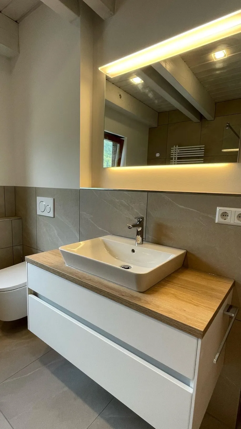 Ein modernes Badezimmer mit einem schwebenden Waschtisch in Weiß und einer Holzplatte, auf der ein eckiges Aufsatzwaschbecken platziert ist.