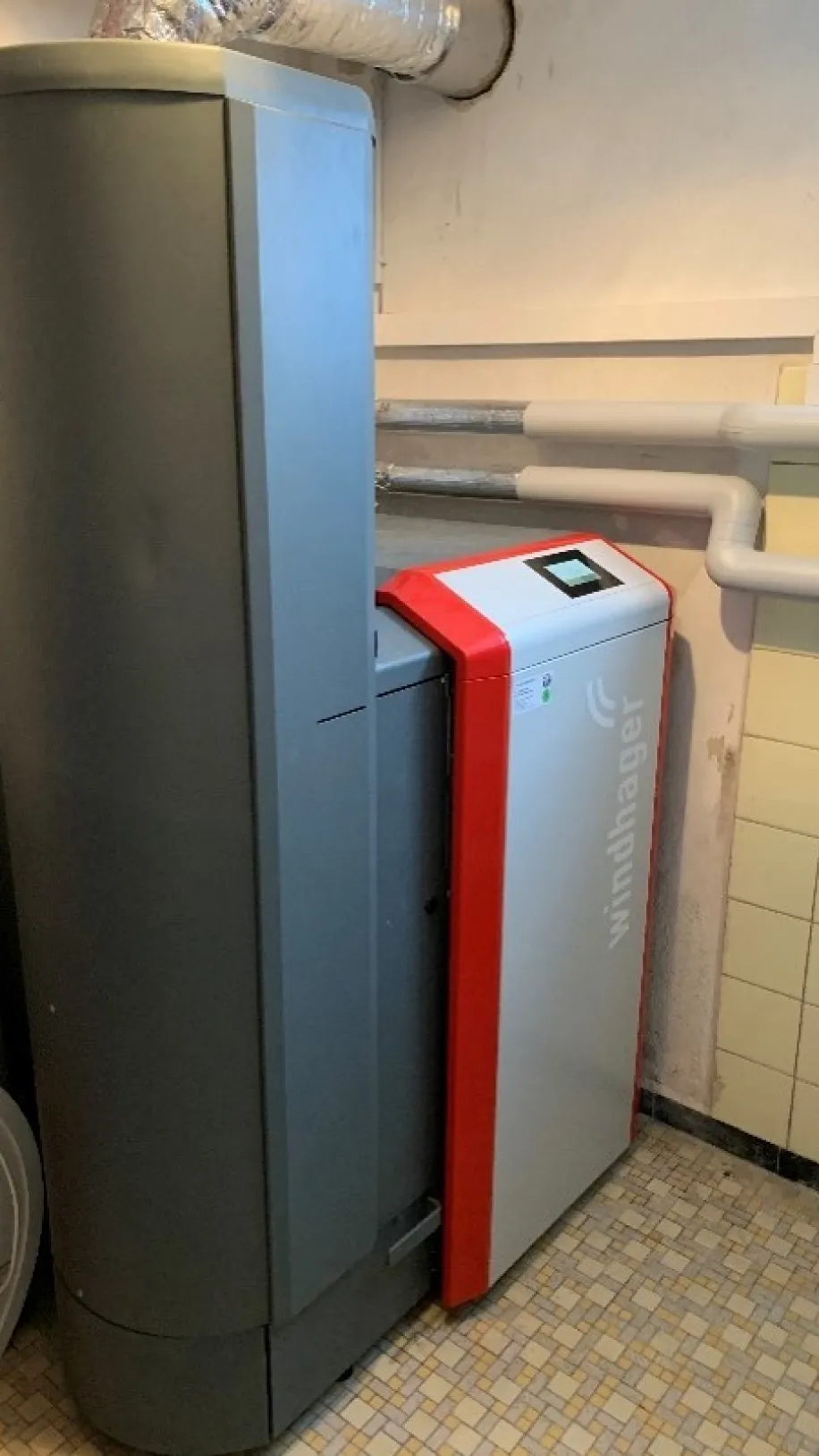 Moderne Heizungsanlage von Windhager in einem Technikraum, mit angeschlossenen Rohrleitungen und digitalem Bedienfeld.