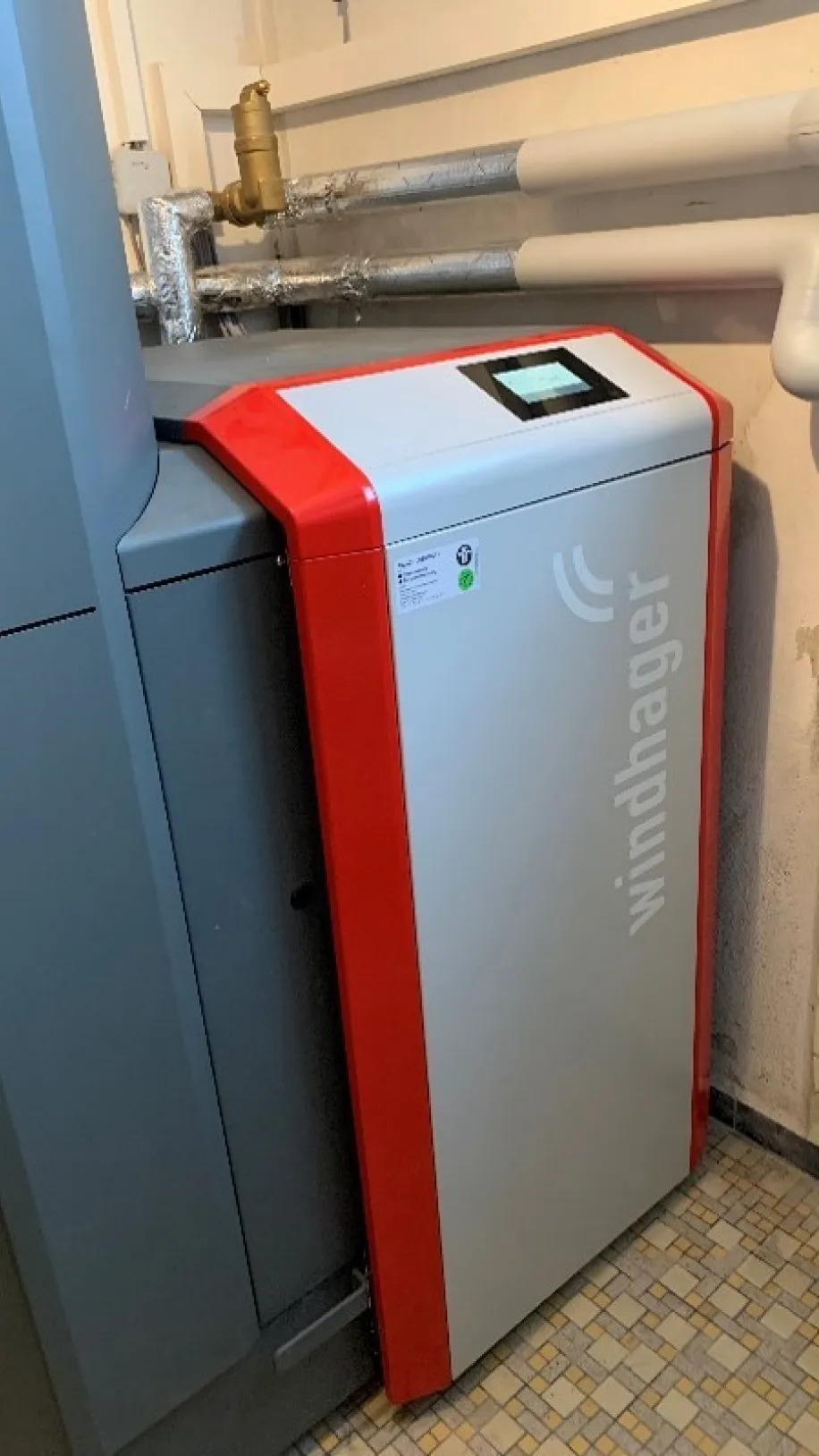 Moderne Heizungsanlage von Windhager in einem Technikraum, mit angeschlossenen Rohrleitungen und digitalem Bedienfeld.