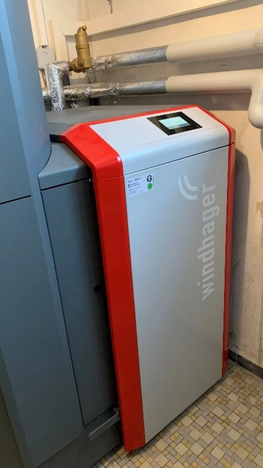 Moderne Heizungsanlage von Windhager in einem Technikraum, mit angeschlossenen Rohrleitungen und digitalem Bedienfeld.