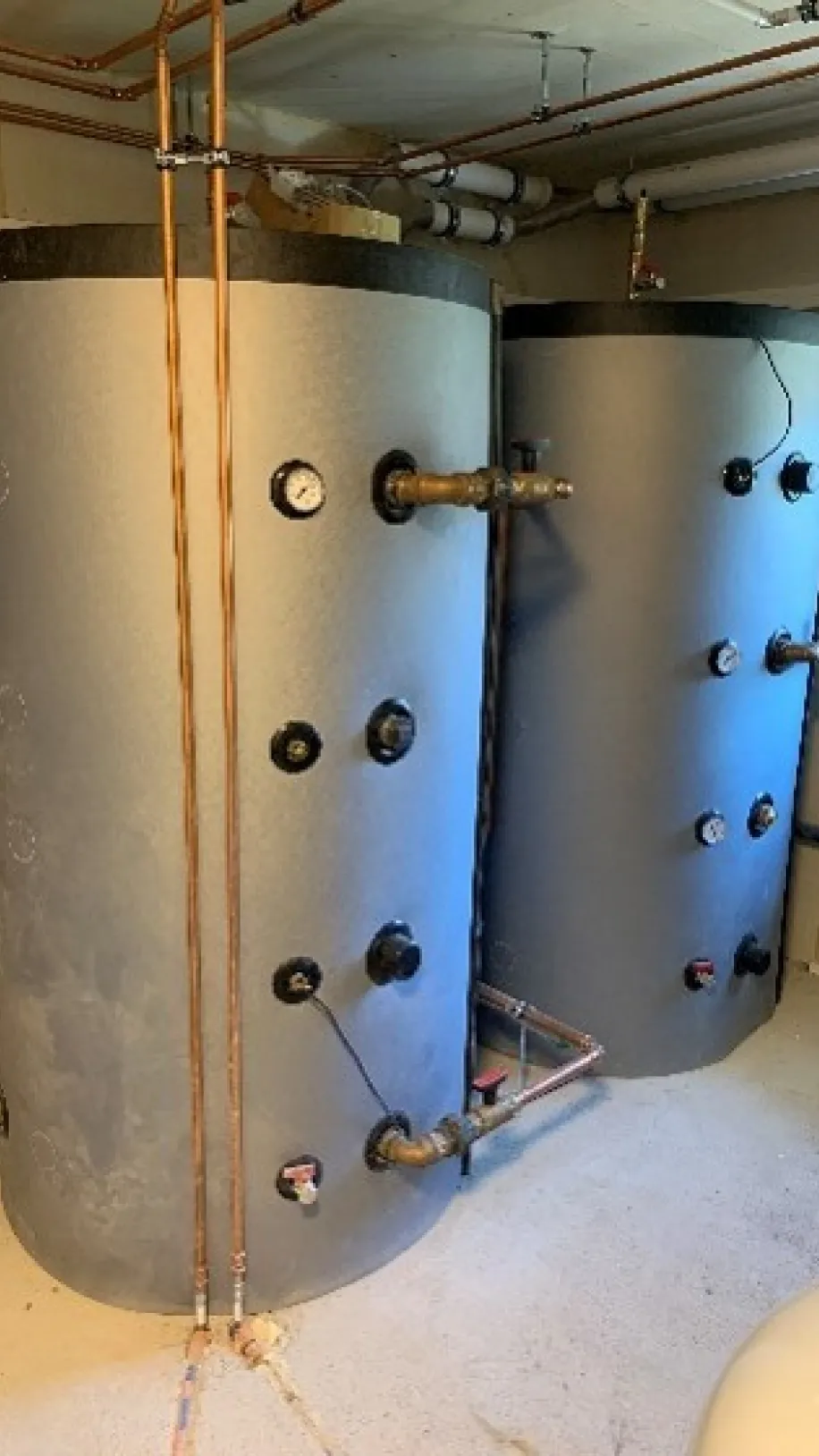 Zwei große Pufferspeicher im Heizraum mit angeschlossenen Kupferrohren, Teil einer modernen Heizungsanlage im Keller.