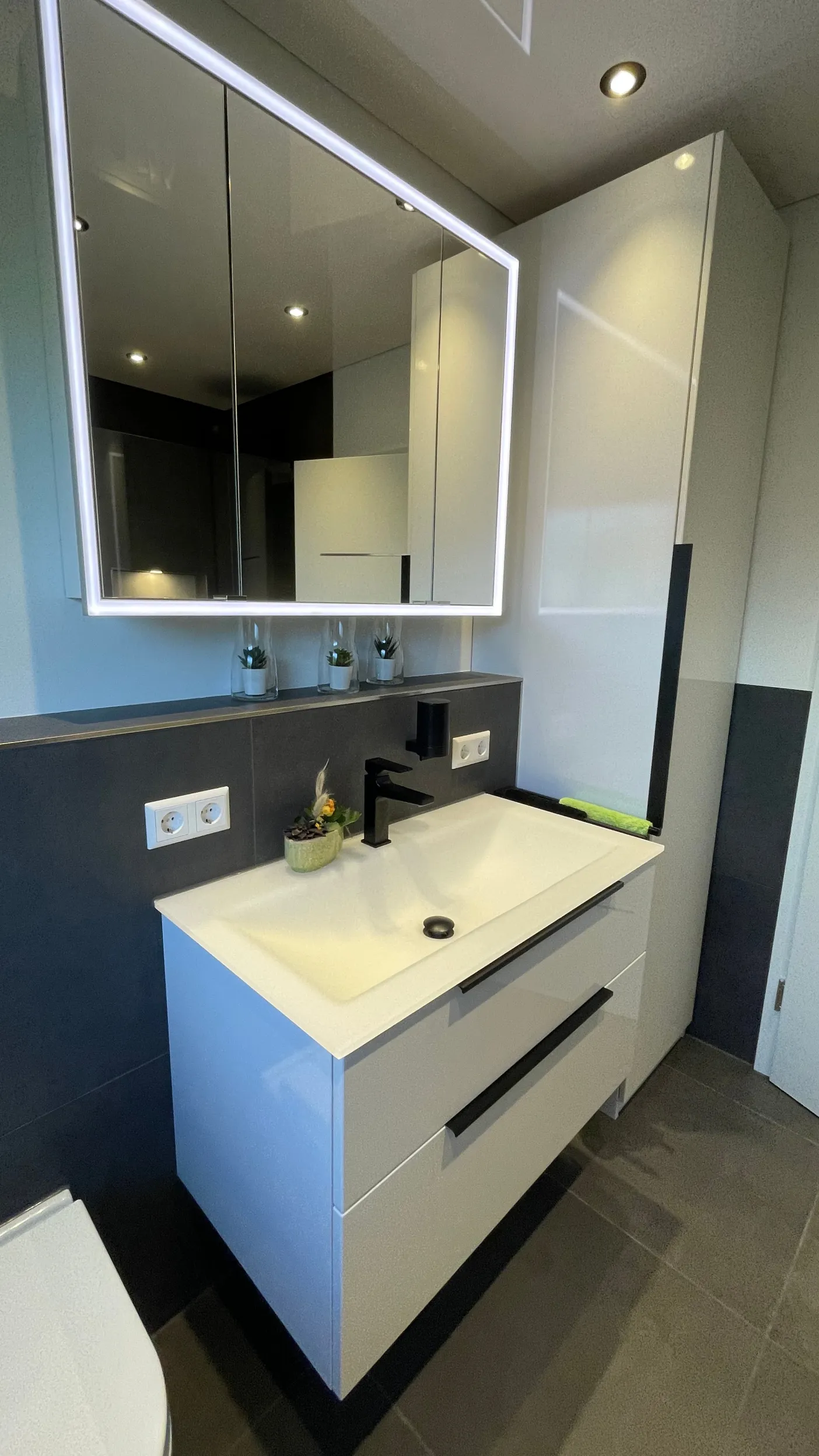 Ein modernes Badezimmer mit einem weißen Waschtisch mit zwei großen Schubladen und einem schwarzen Wasserhahn.