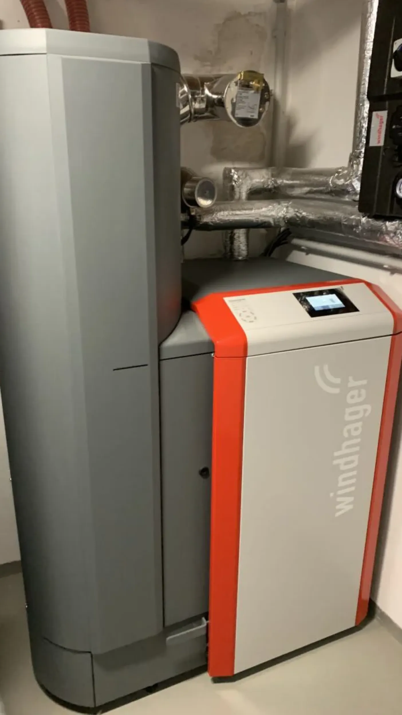 Moderne Pelletheizung der Marke Windhager in einem Heizungsraum, mit isolierten Rohrleitungen und digitalem Steuerungsdisplay.