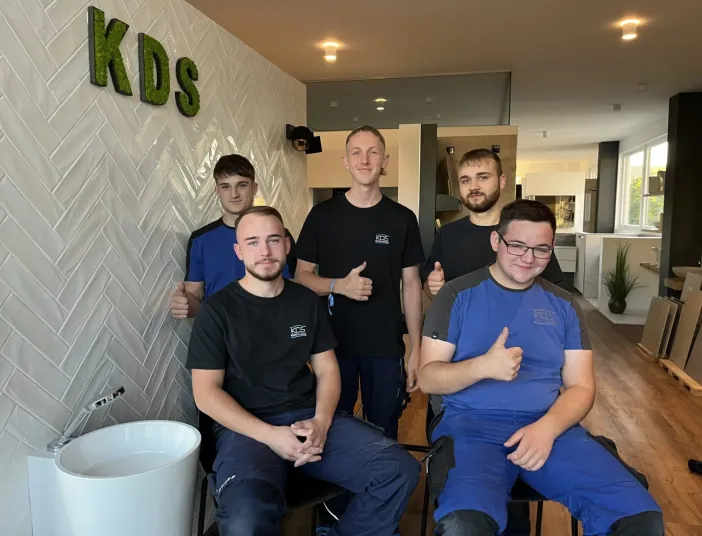 Fünf junge Auszubildende von KDS-Haustechnik posieren mit Daumen nach oben in der Badausstellung.